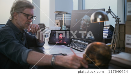 Scientist uses tablet and computer with 3D visualization of ancient extinct human head 117640624
