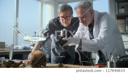 Paleoanthropologist and archaeologist take picture of skull remains with camera 117640633