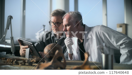 Mature archaeologist uses tablet computer and talks to colleague 117640648