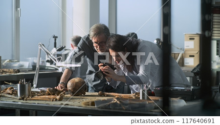 Female paleoanthropologist takes photo of fossil skull remains with colleague 117640691