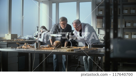 Senior paleoanthropologist takes photo of fossil remains with colleague 117640700