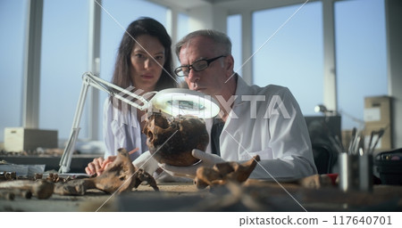 Senior paleoanthropologist examines fossil remains of bones, shows to female scientist Senior paleoanthropologist examines fossil remains of bones, shows to female scientist 117640701