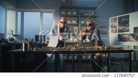 Two archaeologists in VR headsets study remains of ancient extinct human skeleton 117640707