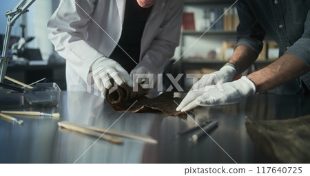 Two archaeologists unroll ancient Egyptian papyrus on table 117640725