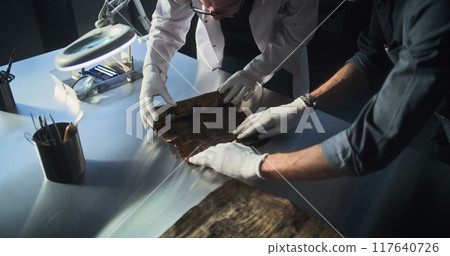 Two archaeologists carefully roll out ancient Egyptian papyrus on the table 117640726