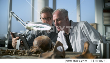 Mature archaeologist uses tablet computer and talks to colleague 117640760