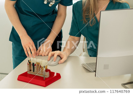 Dentists implantologists look at the computer. On the table there is a model with teeth implants 117640769