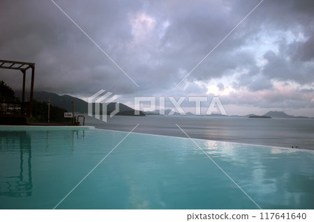 Young woman watching sunrise at a resort with a swimming pool overlooking the sea in Yeosu Young woman watching sunrise at a resort with a swimming pool overlooking the sea in Yeosu 117641640