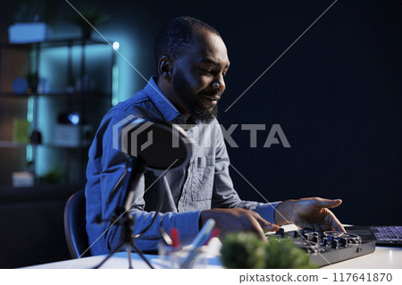 Artist filming DJ mixing tutorial in apartment studio, showing examples of sampling on sound controller to viewers. Entertainer showing modern musical equipment to subscribers in living room 117641870