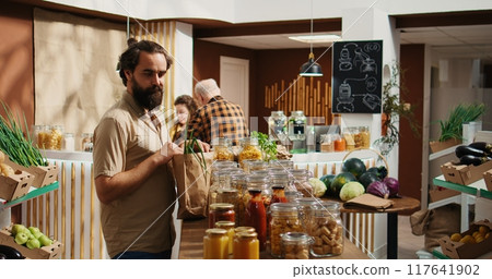 Jib up shot of man in zero waste supermarket using biodegradable paper bag while shopping for pantry staples. Client in local shop using no single use plastics policy and renewable energy Jib up shot of man in zero waste supermarket using biodegradable paper bag while shopping for pantry staples. Client in local shop using no single use plastics policy and renewable energy 117641902
