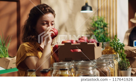 Vegan woman in eco friendly zero waste supermarket counting apples, adding them to shopping basket. Client in local neighborhood grocery shop picking farm grown handpicked fruits 117641926