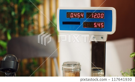 Close up of electronic scale in zero waste supermarket with low carbon dioxide emissions. Panning shot of weighing machine in local grocery store used for bulk products, fruits and vegetables Close up of electronic scale in zero waste supermarket with low carbon dioxide emissions. Panning shot of weighing machine in local grocery store used for bulk products, fruits and vegetables 117641930