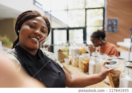 Female blogger creates eco friendly content promoting sustainable, plastic free shopping and healthy living. Vendor filming with smartphone, showcasing trendy tips for low carbon footprint lifestyle. 117641935