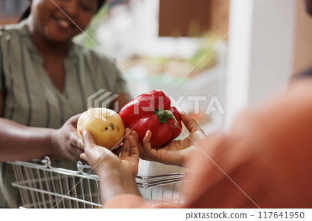 Closeup of merchant at checkout counter in zero waste shop selling fresh vegetables to environmentally conscious customer. Client buys healthy food with no preservatives in local grocery store 117641950