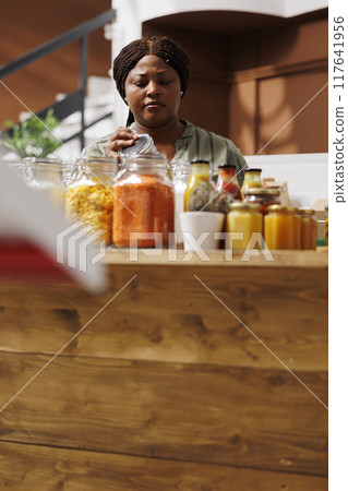 A black woman chef searches for organic and locally grown produce in an eco-friendly supermarket. She values healthy living and zero waste, using eco-friendly cookware and containers. 117641956