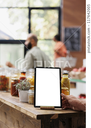 Electronic tablet with white screen is placed in the foreground. It is on a table that is filled with several organic bulk products in reusable jars and containers, promoting a zero-waste initiative. Electronic tablet with white screen is placed in the foreground. It is on a table that is filled with several organic bulk products in reusable jars and containers, promoting a zero-waste initiative. 117642005