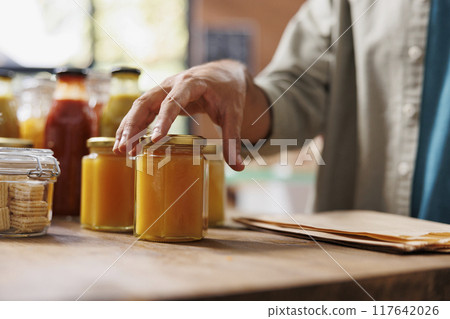 Close-up of person touching jars of nutritious honey in a zero-waste store. Product manufactured from ethically kept bees is available in an environmentally friendly neighborhood store. 117642026