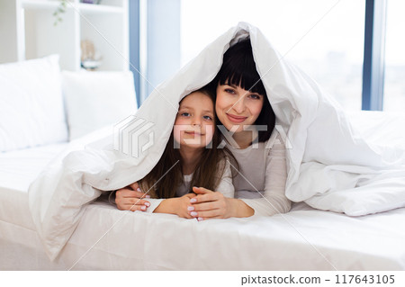 Mother and daughter playing in bed under blanket Mother and daughter playing in bed under blanket 117643105