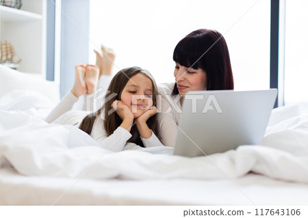 Mother and daughter using laptop together in bed Mother and daughter using laptop together in bed 117643106