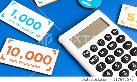 Calculator and toy money on a blue background - Image material for expenses and payments Calculator and toy money on a blue background - Image material for expenses and payments 117643572