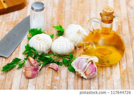 On table there are several cloves of garlic, parsley and small glass decanter with olive oil 117644726