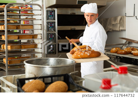 Baker taking out from oven baked bread 117644732