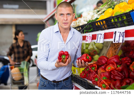 Man choosing red peppers on shelves at farmers market 117644756