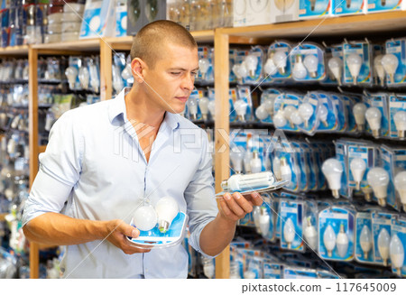 Positive man chooses new bulbs in lighting shop closeup Positive man chooses new bulbs in lighting shop closeup 117645009