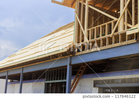 Installing plywood on wooden roofing trusses on house under construction with an assembled roof 117646122