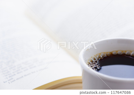 拿著一本打開的書(西洋書)和一個裝有咖啡的咖啡杯,一邊喝咖啡一邊享受閱讀的形象。 拿著一本打開的書(西洋書)和一個裝有咖啡的咖啡杯,一邊喝咖啡一邊享受閱讀的形象。 117647086