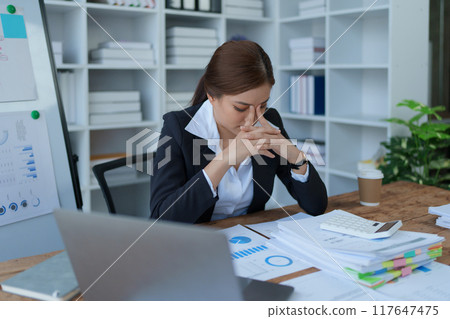 businesswoman plans a finance audit, reviewing documents while battling burnout syndrome. 117647475