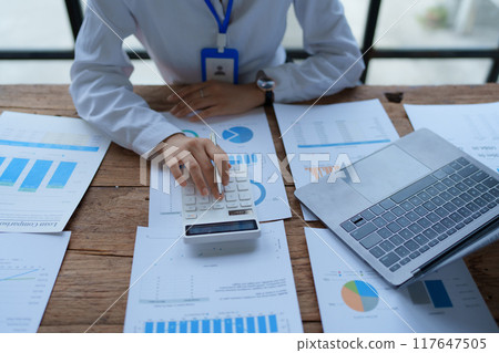 woman meticulously plans a finance audit, using a computer and calculator to review budget documents and ensure accuracy woman meticulously plans a finance audit, using a computer and calculator to review budget documents and ensure accuracy 117647505