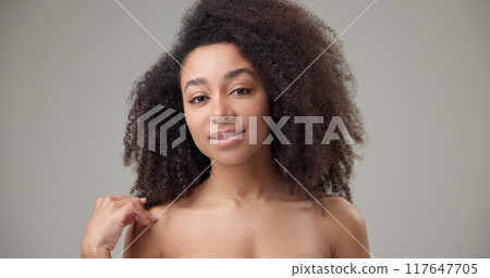 Beauty and healthcare - beautiful African American woman with curly afro hairstyle and clean, healthy skin touching her face, neck, shoulders, looking at the camera with a calm look and a slight smile Beauty and healthcare - beautiful African American woman with curly afro hairstyle and clean, healthy skin touching her face, neck, shoulders, looking at the camera with a calm look and a slight smile 117647705