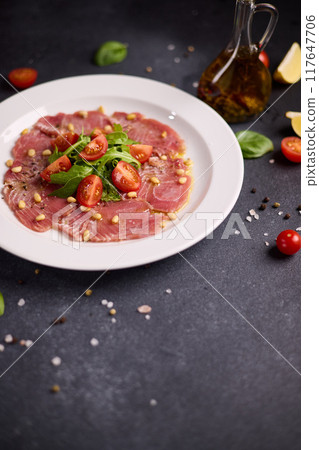 cooking tuna carpaccio - Fresh raw tuna fillet with olive oil and pine nuts on white ceramic plate cooking tuna carpaccio - Fresh raw tuna fillet with olive oil and pine nuts on white ceramic plate 117647706