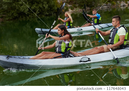 A group of friends enjoying having fun and kayaking while exploring the calm river, surrounding forest and large natural river canyons A group of friends enjoying having fun and kayaking while exploring the calm river, surrounding forest and large natural river canyons 117648043