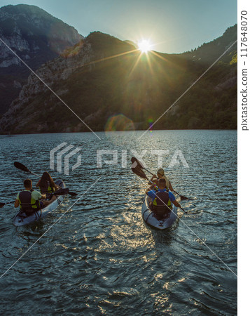 A group of friends enjoying fun and kayaking exploring the calm river, surrounding forest and large natural river canyons during an idyllic sunset. 117648070