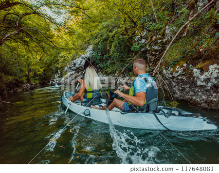 A young couple enjoying an idyllic kayak ride in the middle of a beautiful river surrounded by forest greenery 117648081