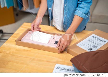 Young online seller man packing his shirt product in the box to ship to his customer from his home studio 117648149