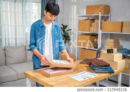 Young online seller man packing his shirt product in the box to ship to his customer from his home studio 117648156
