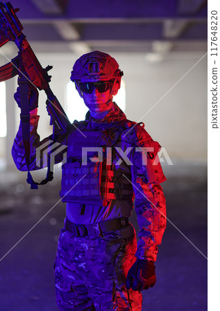 A professional soldier undertakes a perilous mission in an abandoned building illuminated by neon blue and purple lights A professional soldier undertakes a perilous mission in an abandoned building illuminated by neon blue and purple lights 117648220