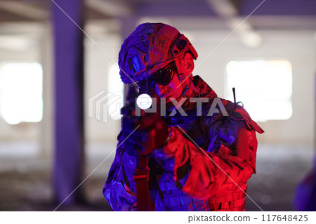 A professional soldier undertakes a perilous mission in an abandoned building illuminated by neon blue and purple lights A professional soldier undertakes a perilous mission in an abandoned building illuminated by neon blue and purple lights 117648425