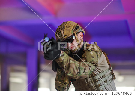 A professional soldier undertakes a perilous mission in an abandoned building illuminated by neon blue and purple lights 117648466