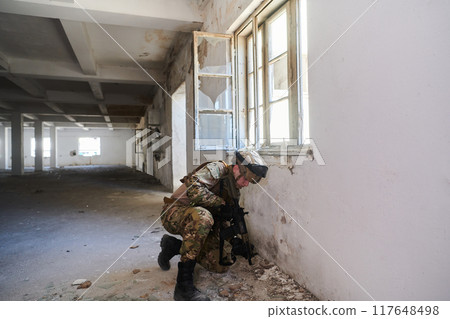 A professional soldier carries out a dangerous military mission in an abandoned building 117648498