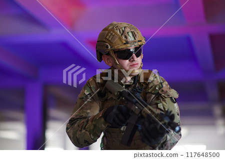 A professional soldier undertakes a perilous mission in an abandoned building illuminated by neon blue and purple lights 117648500
