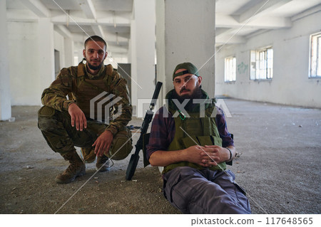 Group of soldiers discusses military tactics while situated in an abandoned building, meticulously planning their moves with focus and determination. Group of soldiers discusses military tactics while situated in an abandoned building, meticulously planning their moves with focus and determination. 117648565