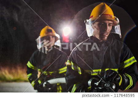 Firefighters using a water hose to eliminate a fire hazard. Team of female and male firemen in dangerous rescue mission.  117648595