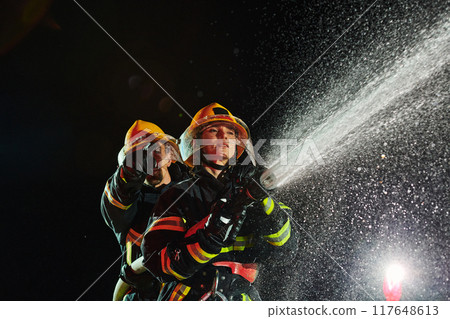 Firefighters using a water hose to eliminate a fire hazard. Team of female and male firemen in dangerous rescue mission. Firefighters using a water hose to eliminate a fire hazard. Team of female and male firemen in dangerous rescue mission. 117648613