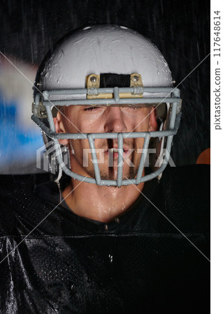 American Football Field: Lonely Athlete Warrior Standing on a Field Holds his Helmet and Ready to Play. Player Preparing to Run, Attack and Score Touchdown. Rainy Night with Dramatic Fog, Blue Light 117648614