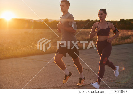 A handsome young couple running together during the early morning hours, with the mesmerizing sunrise casting a warm glow, symbolizing their shared love and vitality 117648621