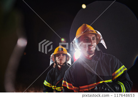 Firefighters using a water hose to eliminate a fire hazard. Team of female and male firemen in dangerous rescue mission.  117648653